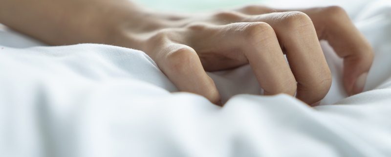 A person is holding their hand on the bed