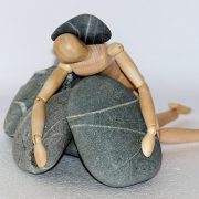 A wooden doll is sitting on top of some rocks
