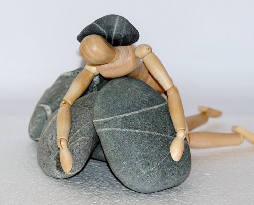 A wooden doll is sitting on top of some rocks