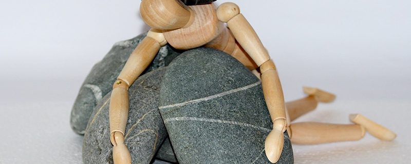 A wooden doll is sitting on top of some rocks