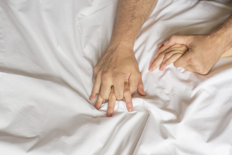A couple of hands touching each other on top of a bed.